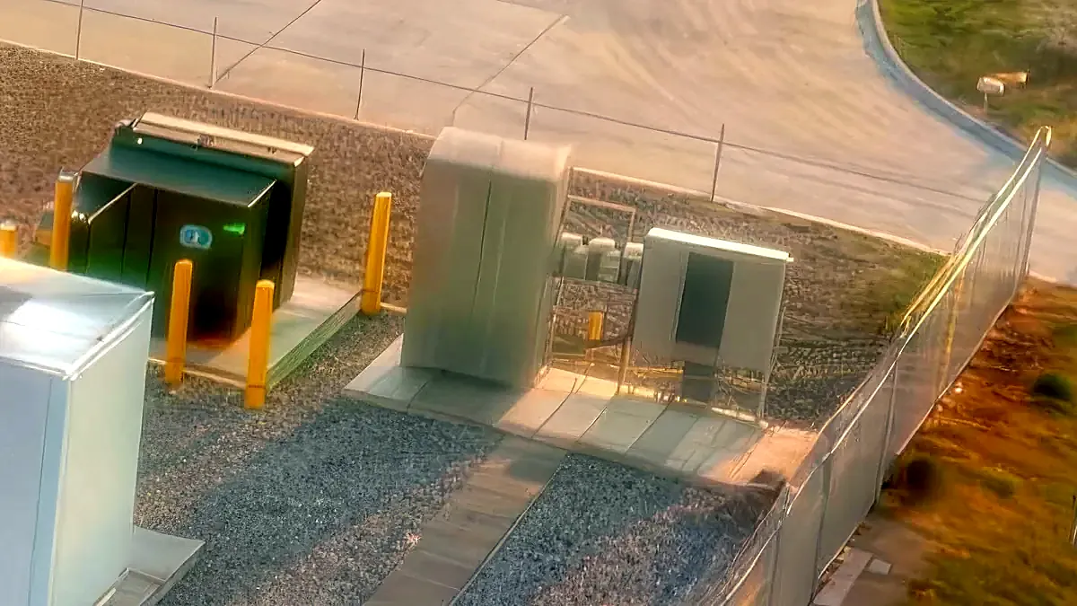 Rendered detail of pad-mount gear beside battery enclosures inside the fence line.